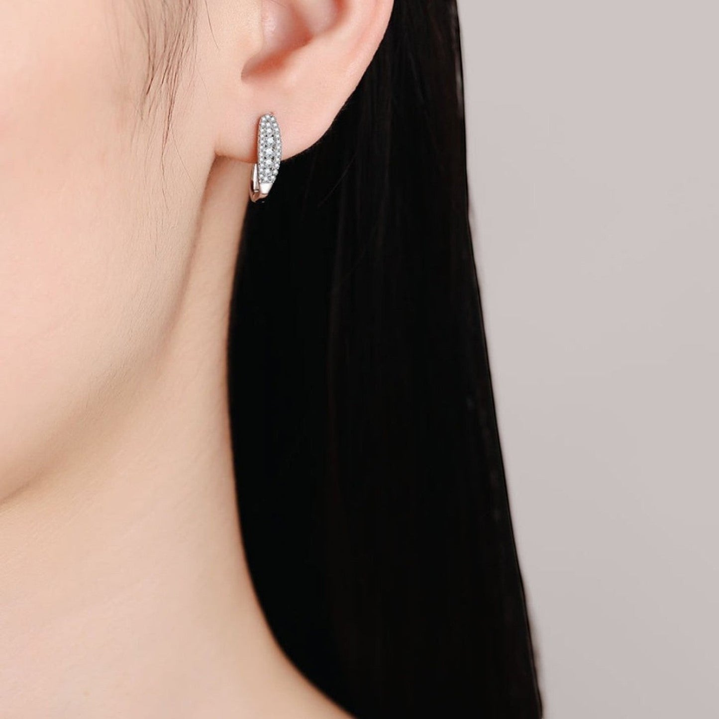 Zijaanzicht van een model dat de zilveren ModaMelhor ovalen moissanite huggie oorbel met sprankelende steentjes in het oor draagt.