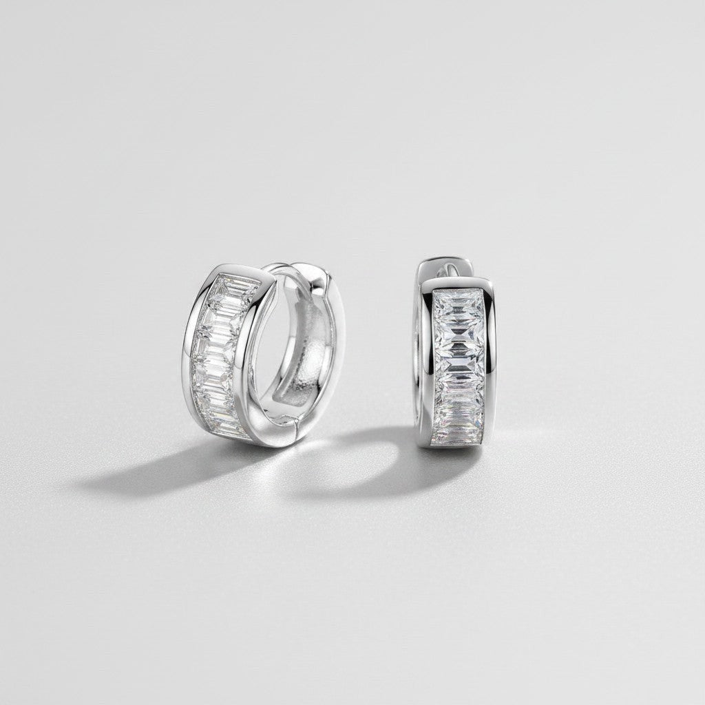Vooraanzicht en zijaanzicht van de platliggende ModaMelhor 1.8 karaat baguette moissanite huggie oorbellen van gerhodineerd 925 sterling zilver met een strakke kanaalzetting.