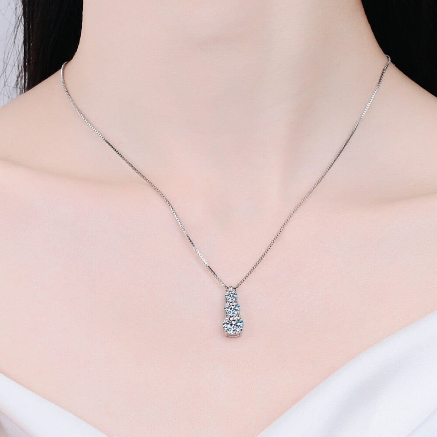 Vooraanzicht van een model dat de zilverkleurige ModaMelhor 925 sterling zilveren ketting met de verticale driestenen moissanite hanger om de hals draagt.