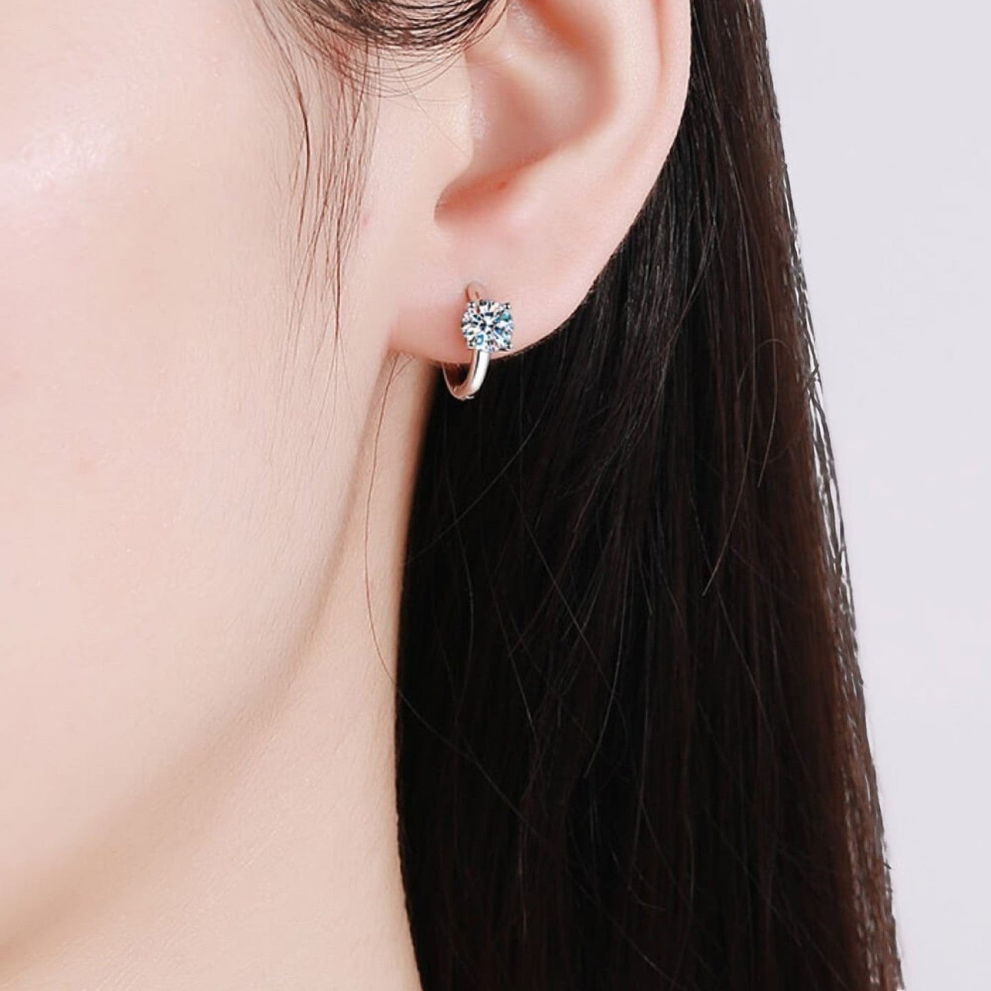 Sfeerfoto van een model die de zilveren ModaMelhor huggie oorbel met een sprankelende, centraal geplaatste moissanite steen elegant in het oor draagt.