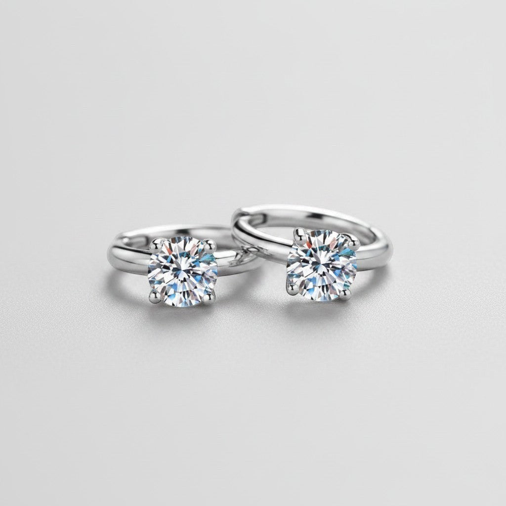 Vooraanzicht van de platliggende ModaMelhor huggie oorbellen van 925 sterling zilver met twee centraal geplaatste, sprankelende moissanite stenen.