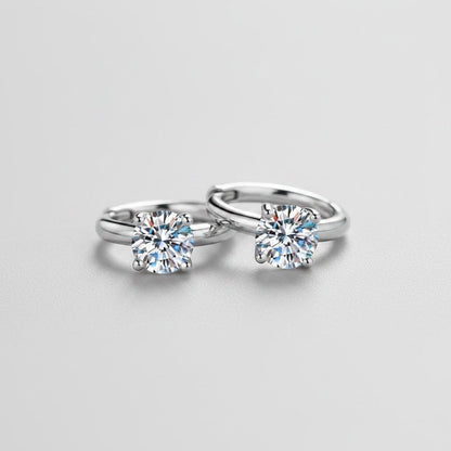 Vooraanzicht van de platliggende ModaMelhor huggie oorbellen van 925 sterling zilver met twee centraal geplaatste, sprankelende moissanite stenen.