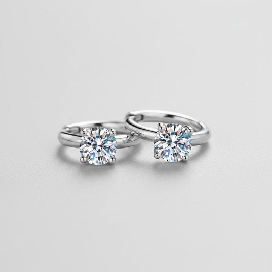 Vooraanzicht van de platliggende ModaMelhor huggie oorbellen van 925 sterling zilver met twee centraal geplaatste, sprankelende moissanite stenen.
