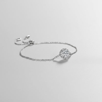 Zijaanzicht van de ModaMelhor zilveren armband liggend op een lichtgrijze ondergrond, met de nadruk op de verhoogde zetting van de glanzende 1 karaat moissanite steen.