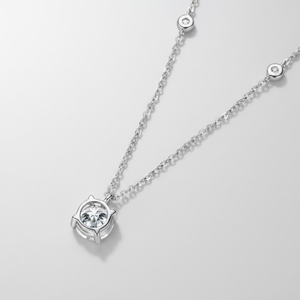 Close-up van de ModaMelhor hanger met een ronde 2 karaat moissanite in een vierpootzetting (4-prong), hangend aan een zilveren ketting met subtiele zirkonia accentsteentjes.