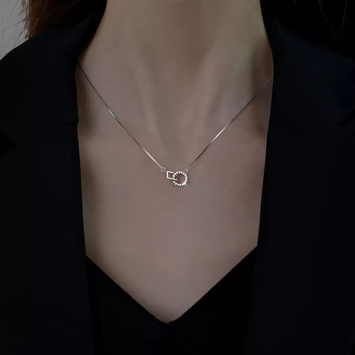 Vooraanzicht van een model dat de zilveren ModaMelhor geometrische ketting met het in elkaar gehaakte vierkant en de zirkonia cirkel om de hals draagt.