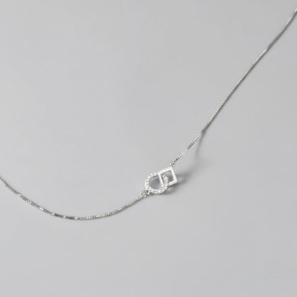 Overzicht van de ModaMelhor zilveren ketting met een geometrische hanger van een in elkaar gehaakt glad vierkant en een met zirkonia bezette cirkel.
