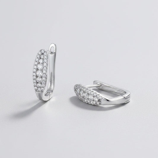 Vooraanzicht en zijaanzicht van de platliggende ModaMelhor ovalen moissanite huggie oorbellen van gerhodineerd 925 sterling zilver bezet met meerdere rijen kleine moissanite stenen.