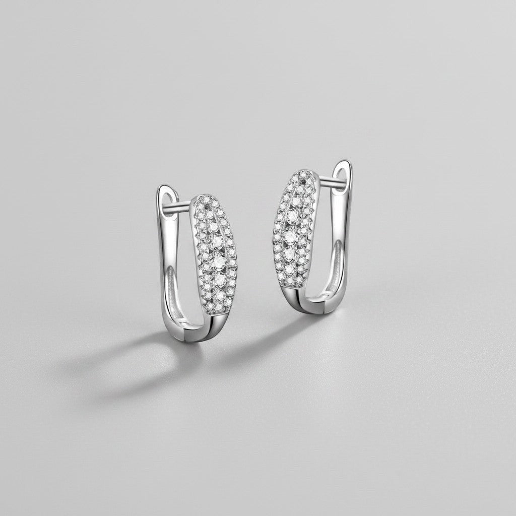 Zijaanzicht van de twee rechtopstaande ModaMelhor ovalen moissanite huggie oorbellen van gerhodineerd 925 sterling zilver met de focus op de sluiting en de schitterende pavézetting.