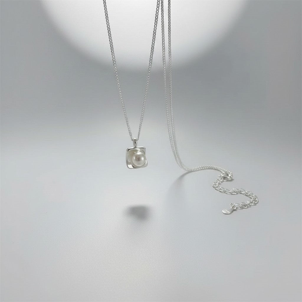Overzicht van de ModaMelhor zilveren ketting met een moderne, vierkante hanger waarin een ronde zoetwaterparel centraal is geplaatst.