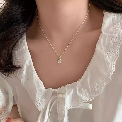Vooraanzicht van een model dat de zilveren ModaMelhor ketting met de organisch gevormde zoetwaterparel hanger om de hals draagt.