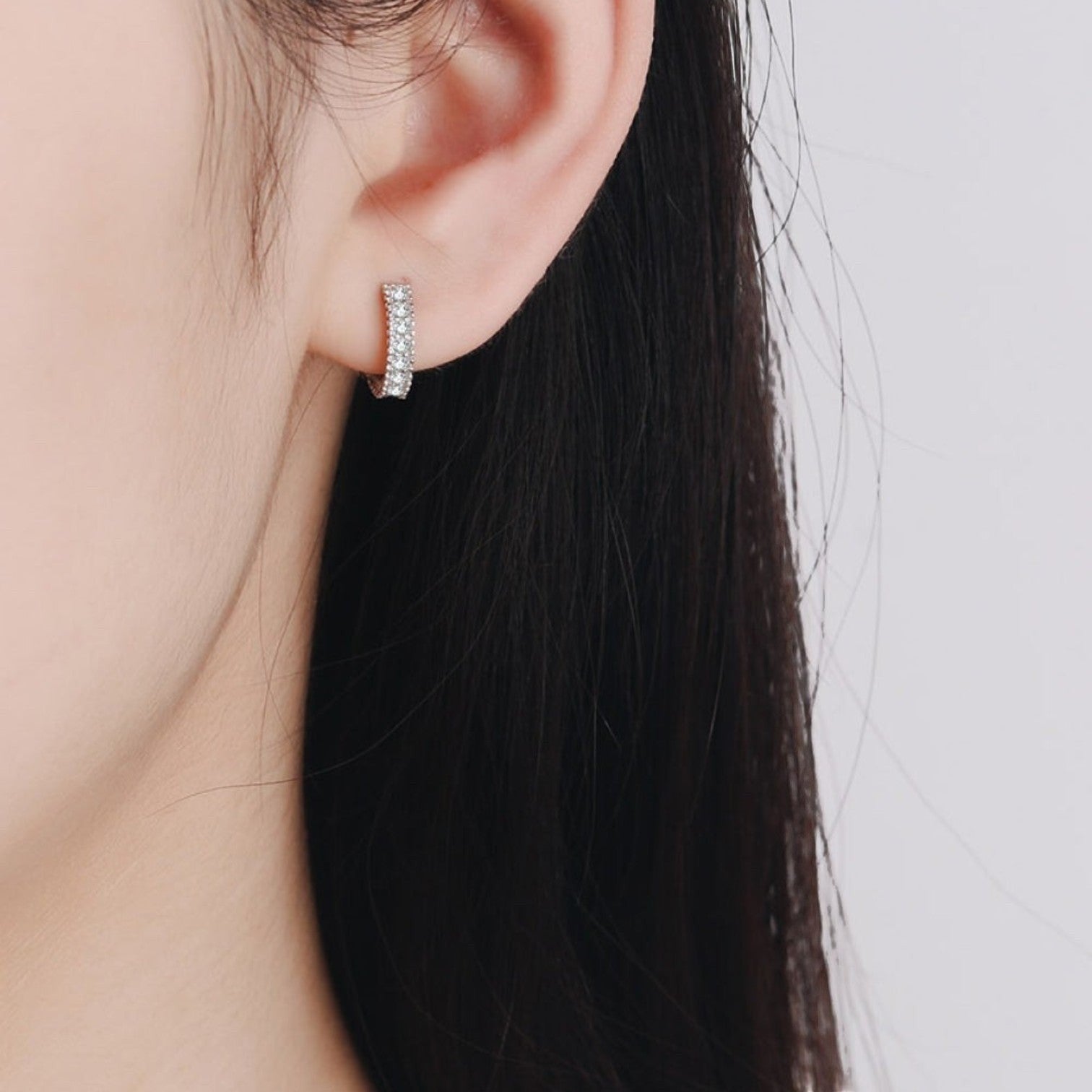 Sfeerfoto van een model die de zilveren ModaMelhor huggie oorbel met een subtiele dubbele rij moissanite steentjes elegant in het oor draagt.