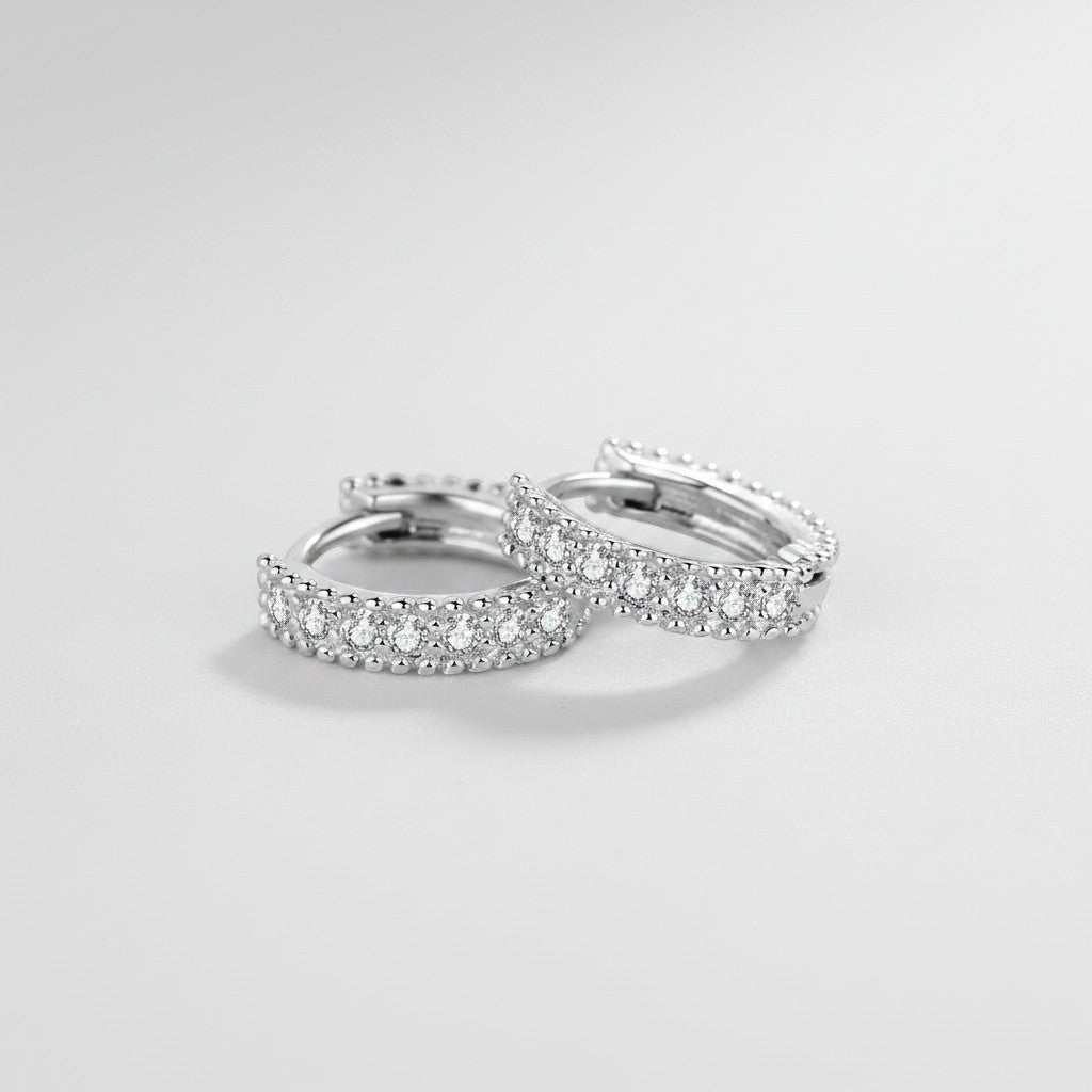 Schuin bovenaanzicht van de platliggende ModaMelhor huggie oorbellen van 925 sterling zilver, ingelegd met een verfijnde dubbele rij sprankelende moissanite steentjes.