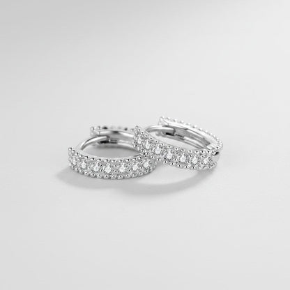 Schuin bovenaanzicht van de platliggende ModaMelhor huggie oorbellen van 925 sterling zilver, ingelegd met een verfijnde dubbele rij sprankelende moissanite steentjes.