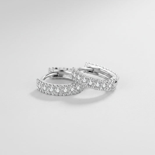 Schuin bovenaanzicht van de platliggende ModaMelhor huggie oorbellen van 925 sterling zilver, ingelegd met een verfijnde dubbele rij sprankelende moissanite steentjes.