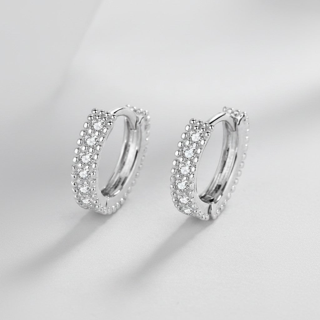 Symmetrisch vooraanzicht van het paar rechtopstaande ModaMelhor huggie oorbellen van 925 sterling zilver met een dubbele rij fonkelende moissanite stenen.