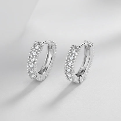 Symmetrisch vooraanzicht van het paar rechtopstaande ModaMelhor huggie oorbellen van 925 sterling zilver met een dubbele rij fonkelende moissanite stenen.