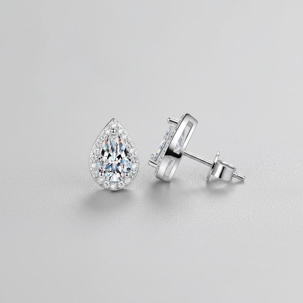 Vooraanzicht en zijaanzicht van de platliggende ModaMelhor druppelvormige oorknopjes van 925 sterling zilver met centrale moissanite stenen en zirkonia accenten.