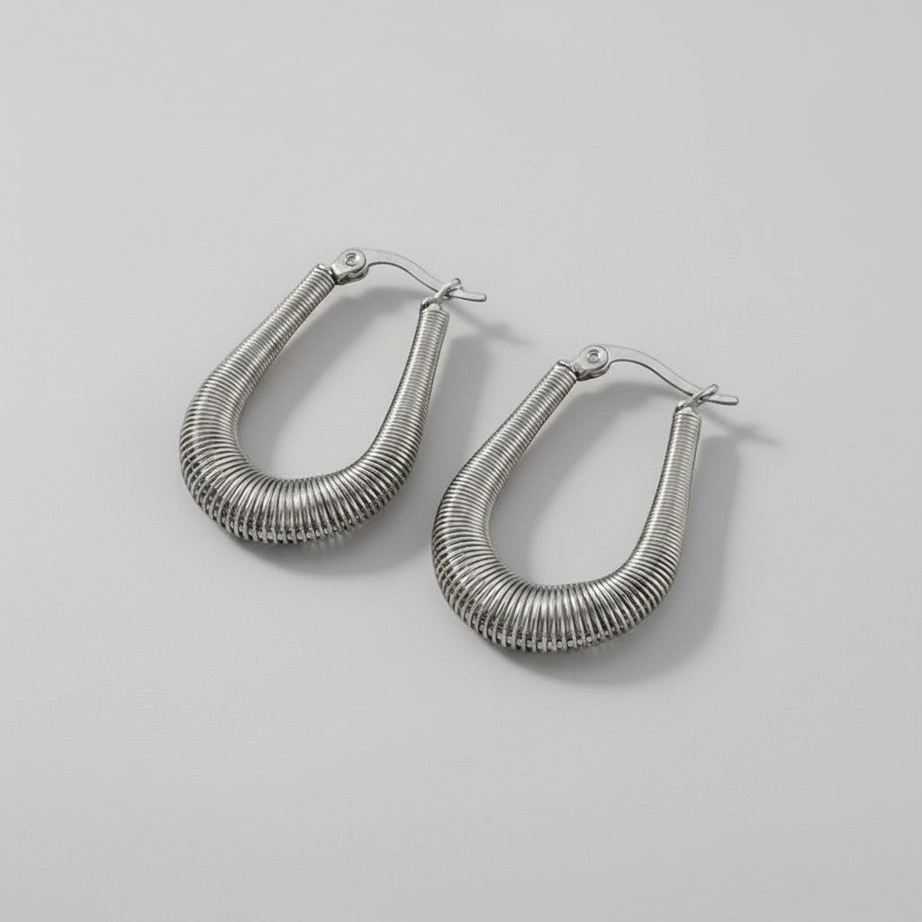 Bovenaanzicht van de twee platliggende ModaMelhor U-shape huggie oorbellen van zilverkleurig titanium, waarbij het fijne ribbelmotief over de gehele ring goed zichtbaar is.