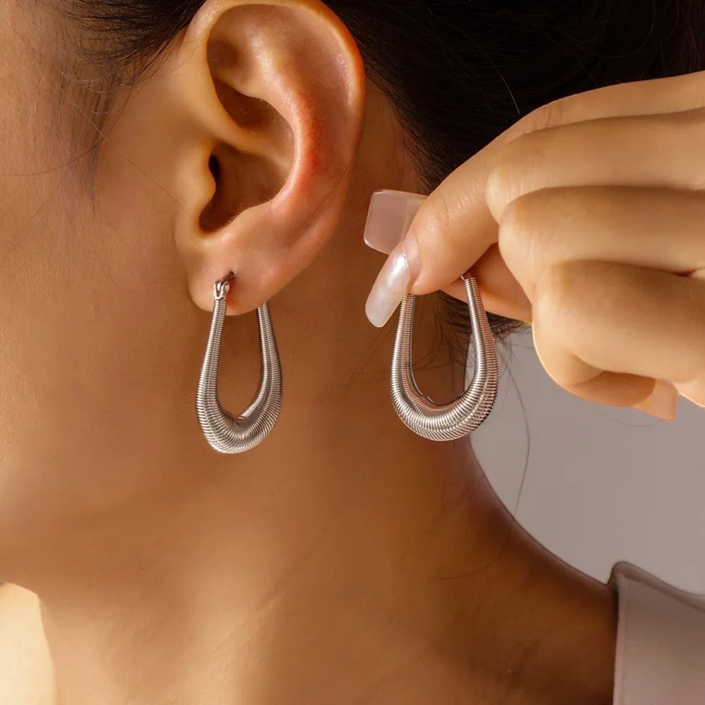 Zijaanzicht van een model dat de zilverkleurige ModaMelhor titanium U-shape huggie oorbel draagt, terwijl de andere oorbel wordt vastgehouden om het ribbelmotief te tonen.