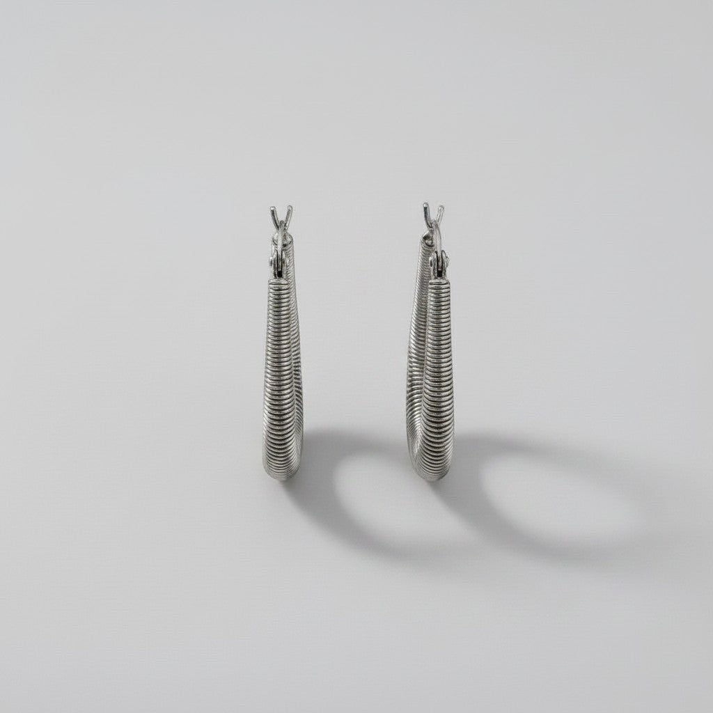 Vooraanzicht van de twee rechtopstaande ModaMelhor U-shape huggie oorbellen van zilverkleurig titanium, voorzien van een fijn horizontaal ribbelmotief.